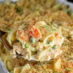 close-up of creamy salmon casserole with peas and carrots on a spoon