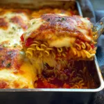Close-up of cheesy ramen lasagna slice being lifted from a baking dish