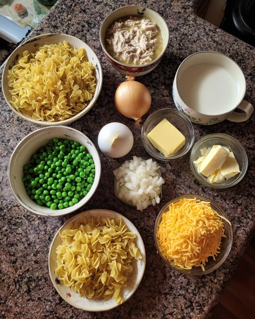 Ingredients for tuna noodle casserole including noodles, peas, tuna, onion, cheese, and milk